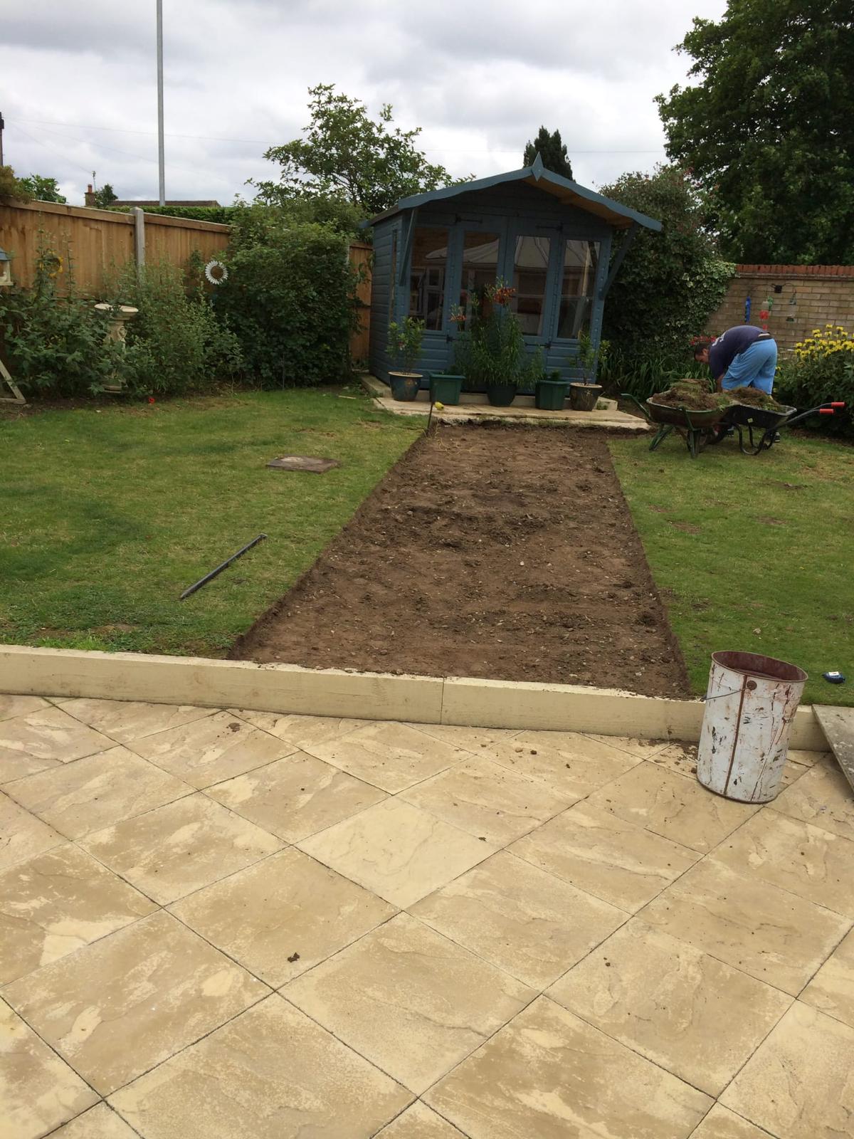 This is a photo of a newly laid patio with a pathway been cut into the grass to form a new slab pathway with a shingle border to the garden shed