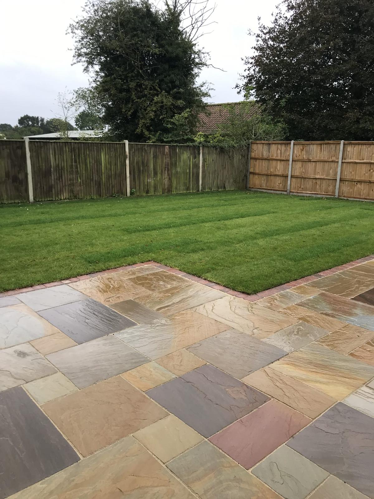 This is a newly installed patio area in grey slabs, with turf grass next to it